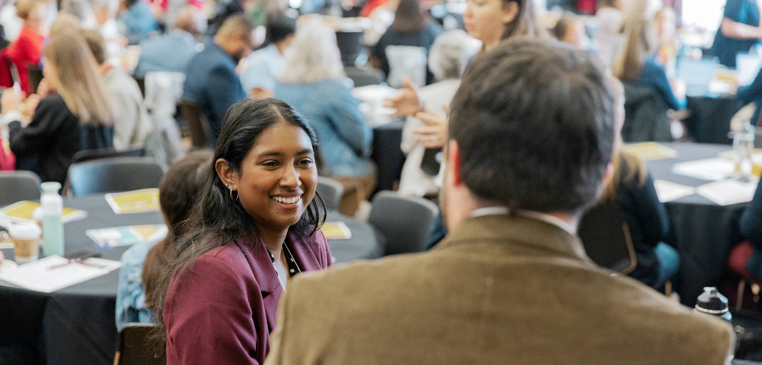 Two people talk at a table in a full conference room.