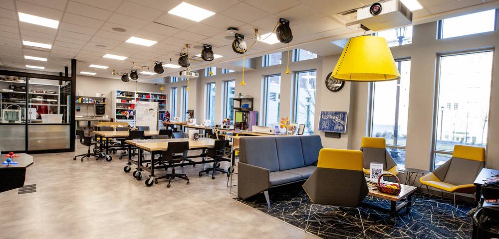 Campus Village 2 Makerspace at the University of South Carolina, featuring collaborative worktables, 3D printers, creative supplies, modern seating, and large windows providing natural light in a vibrant, innovation-focused environment.