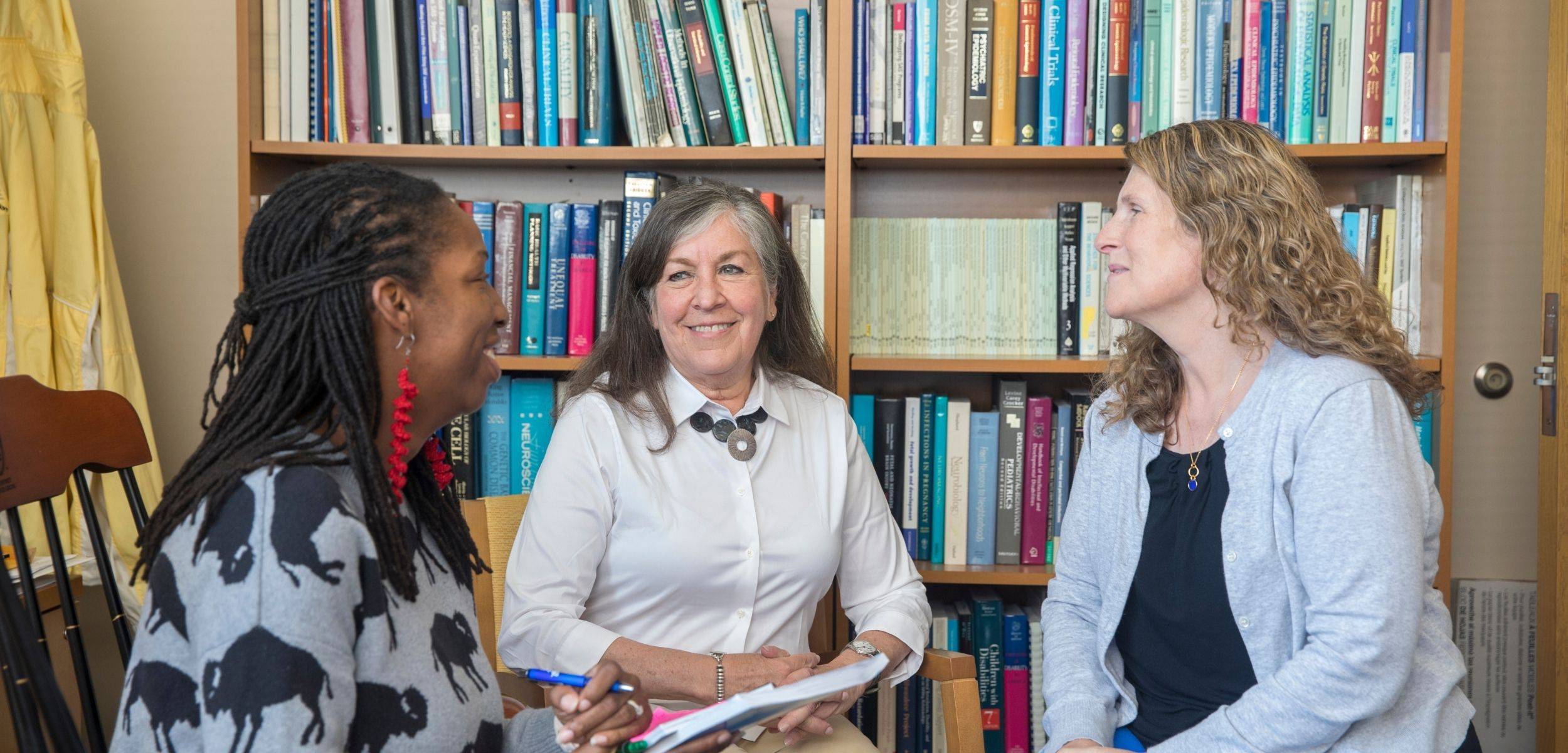 Three women talking in a circle in an office.