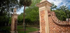 Ornate brick and stone entrance gate surrounded by trees and greenery.