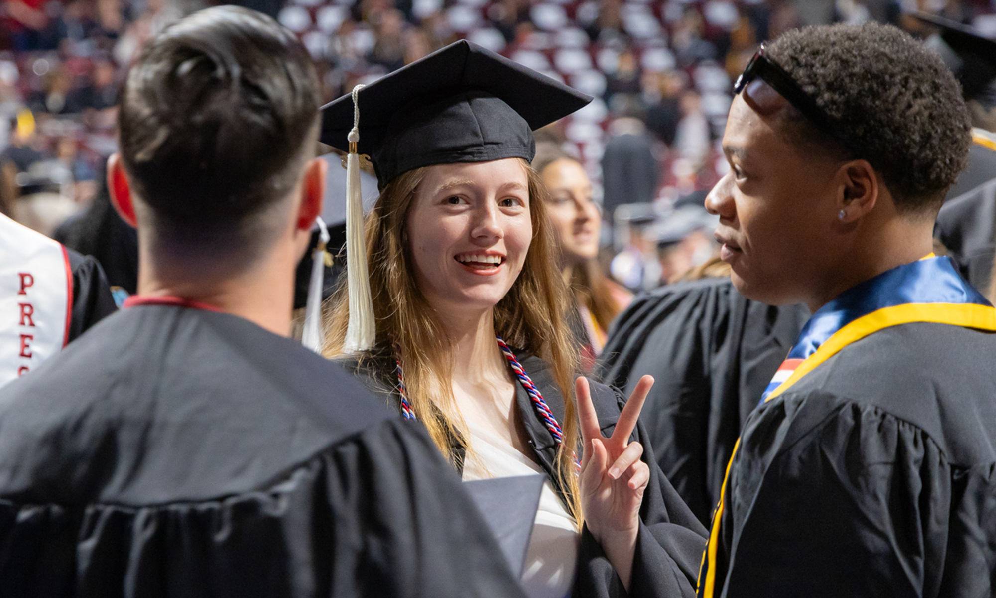 Two graduates in caps and gowns smiling and talking during a commencement ceremony.