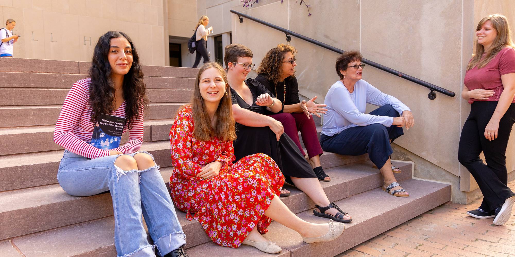 Four women sitting on outdoor steps, smiling and talking together.