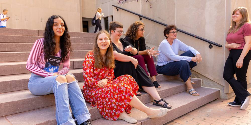 Four women sitting on outdoor steps, smiling and talking together.