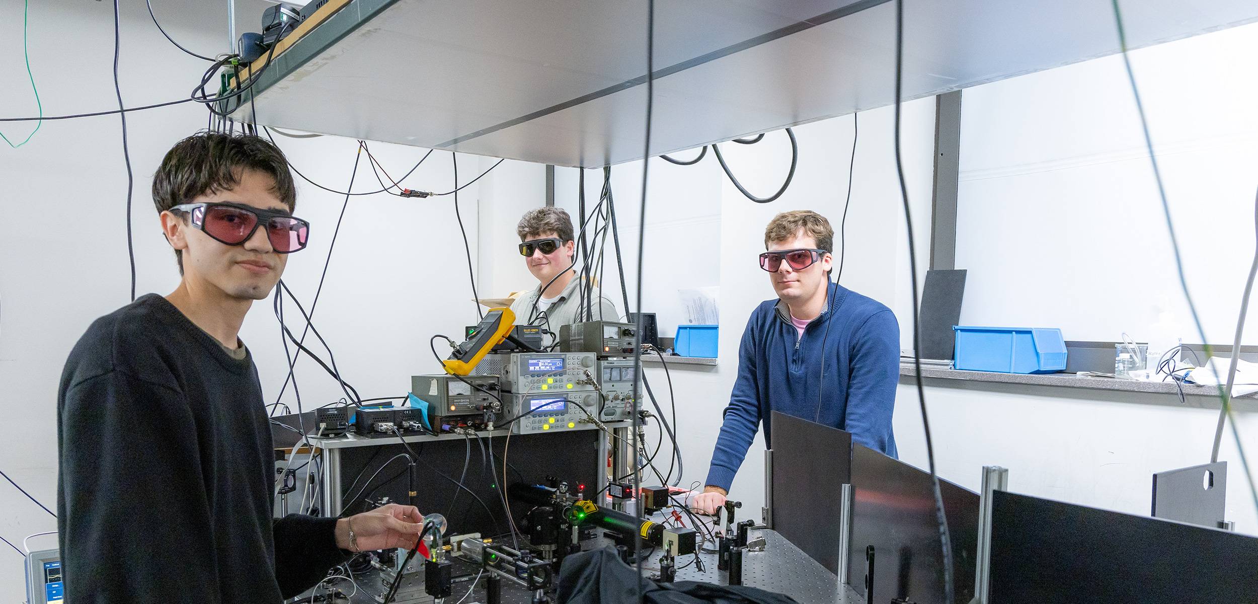 Smiling students wearing safety goggles and a blue lab coat in a science laboratory.