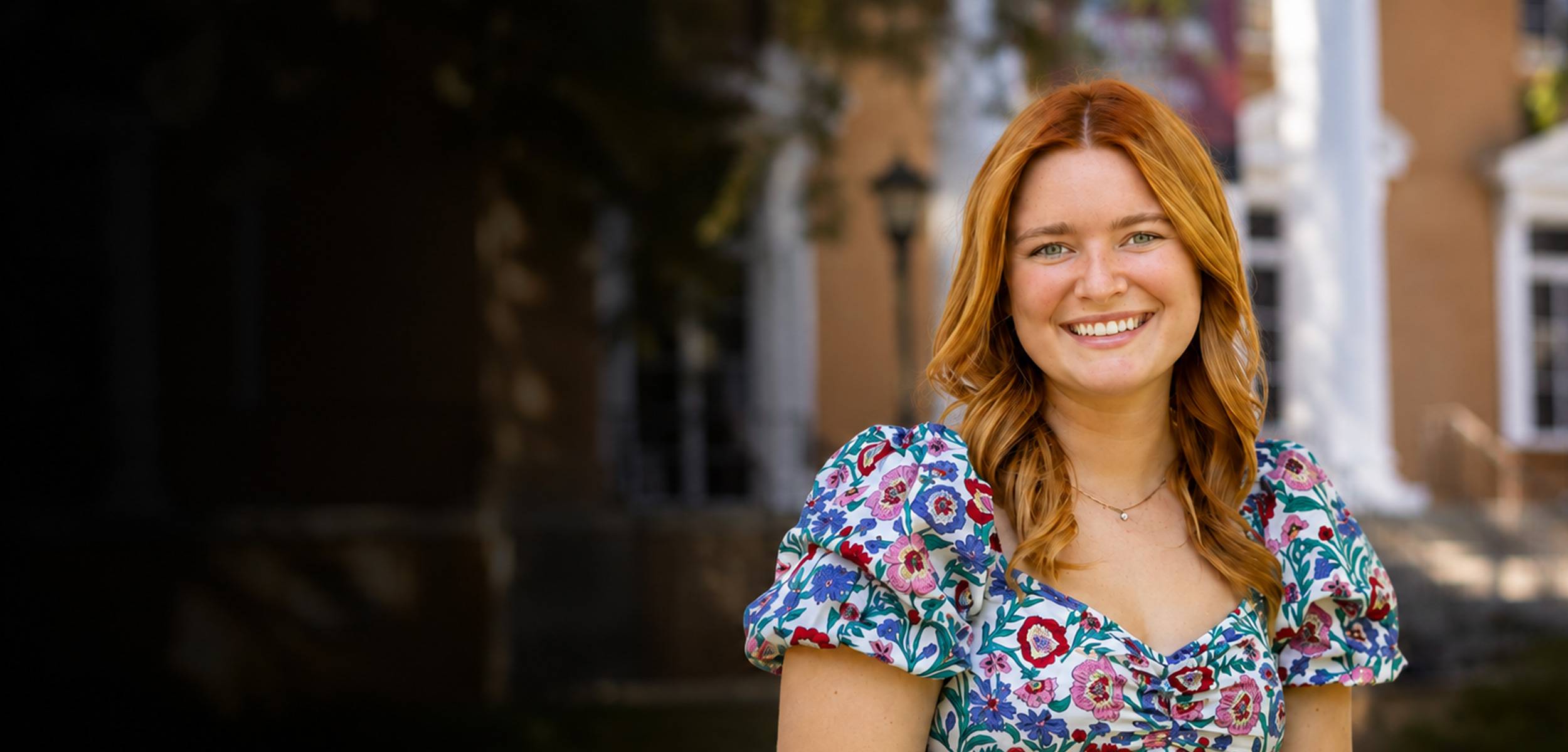 Smiling woman with red hair wearing a colorful floral dress