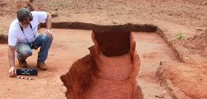Archaeologist kneels beside a deep excavation trench at a South Carolina dig site.