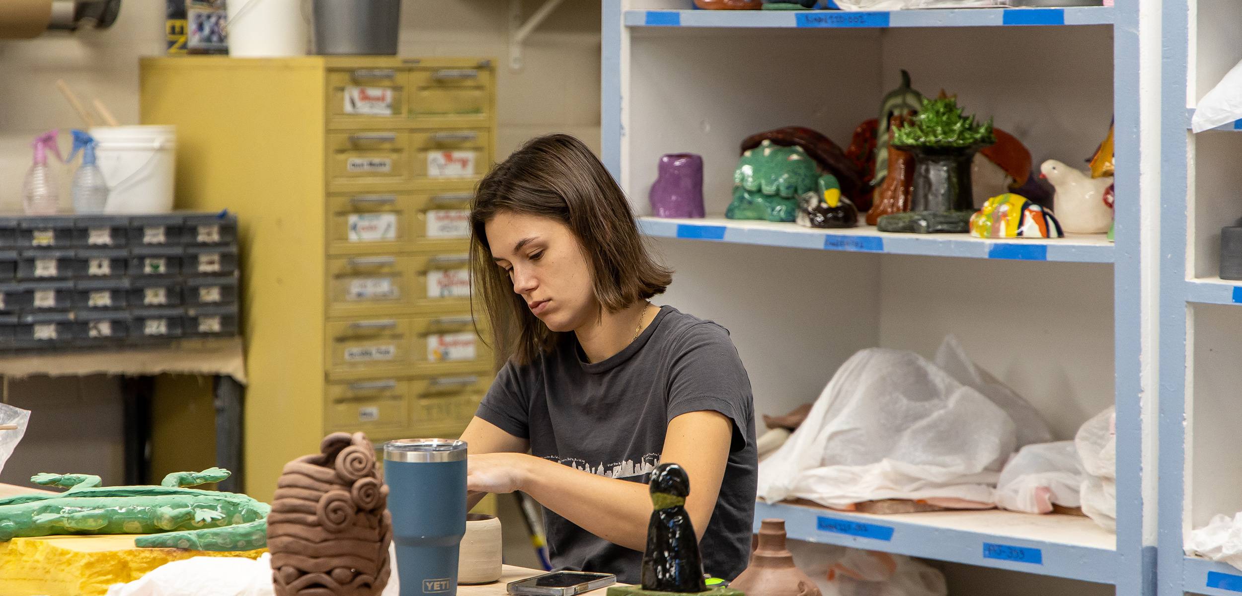 Art student paints a large portrait canvas in a bright studio with other vivid paintings nearby.