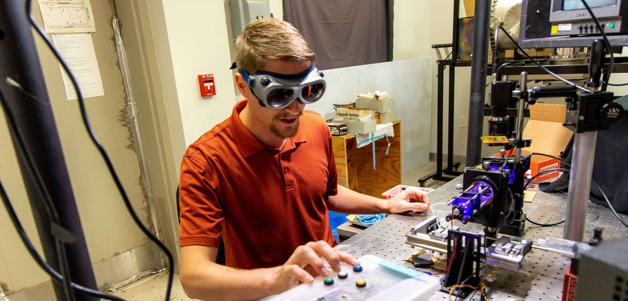 Researcher in safety goggles adjusting equipment in an optics lab