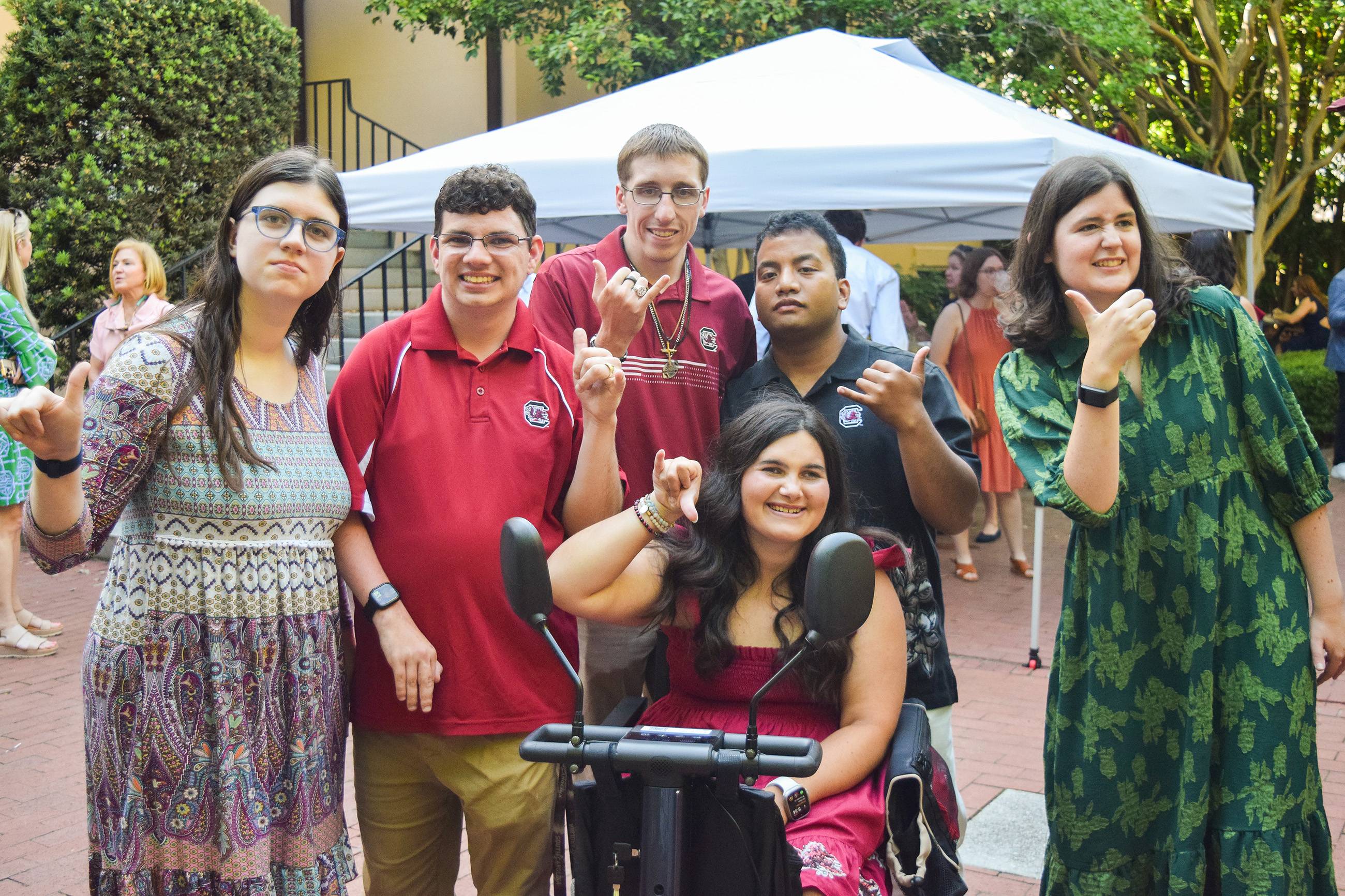 Diverse group of CarolinaLIFE students giving the "Spurs UP" guesture with thumb and pinky.
