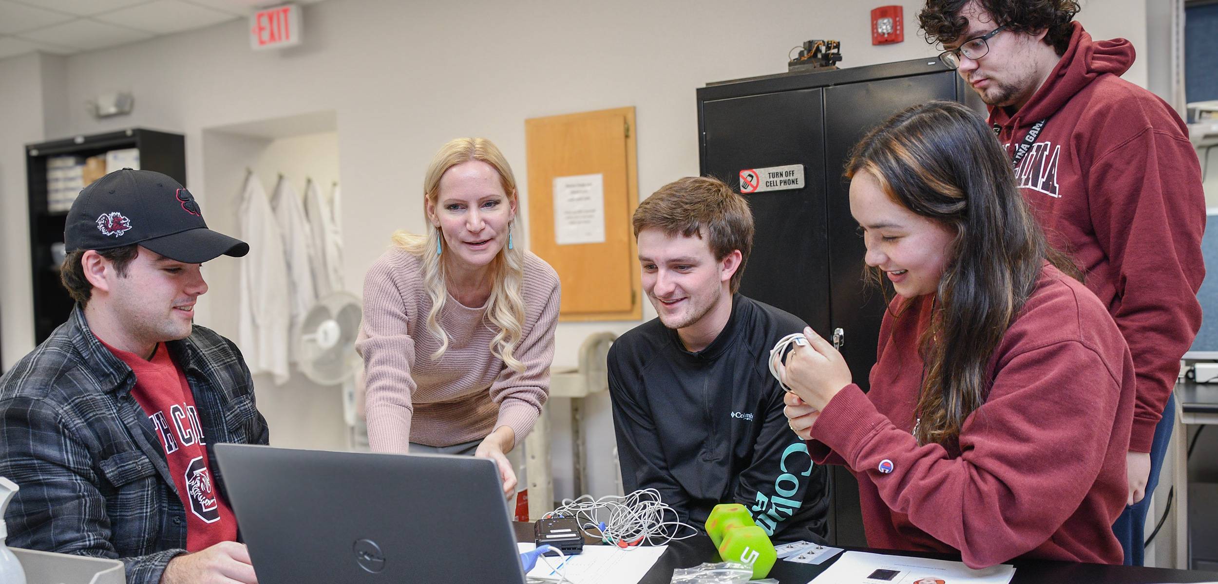 Students and instructor looking at laptop screen in biomedical engineering lab.