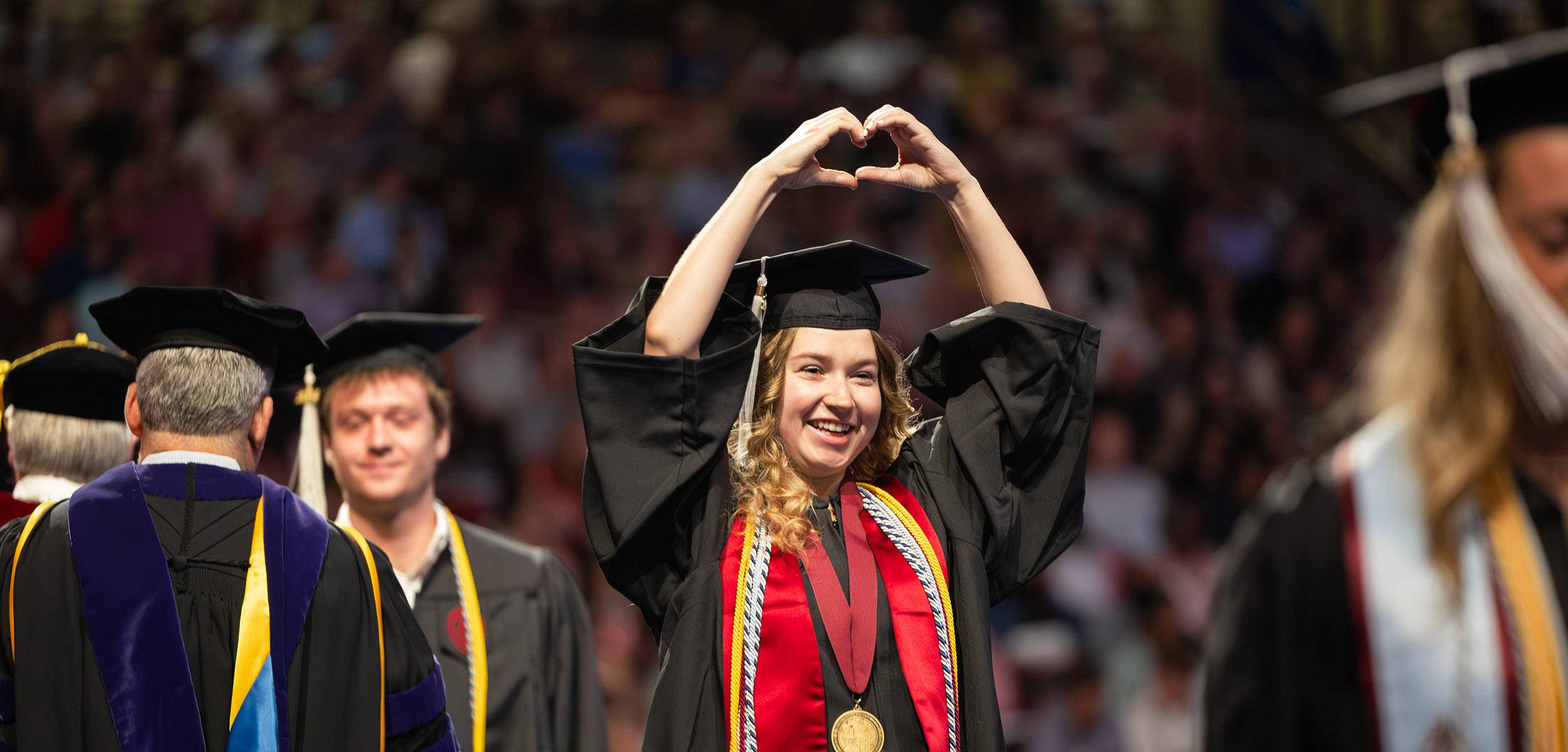 Student holding up their hands in a heart shape during a graduation ceremony