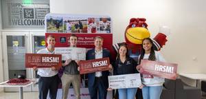 Collin Crick poses with students at an Admitted Student Day event holding HRSM banners.