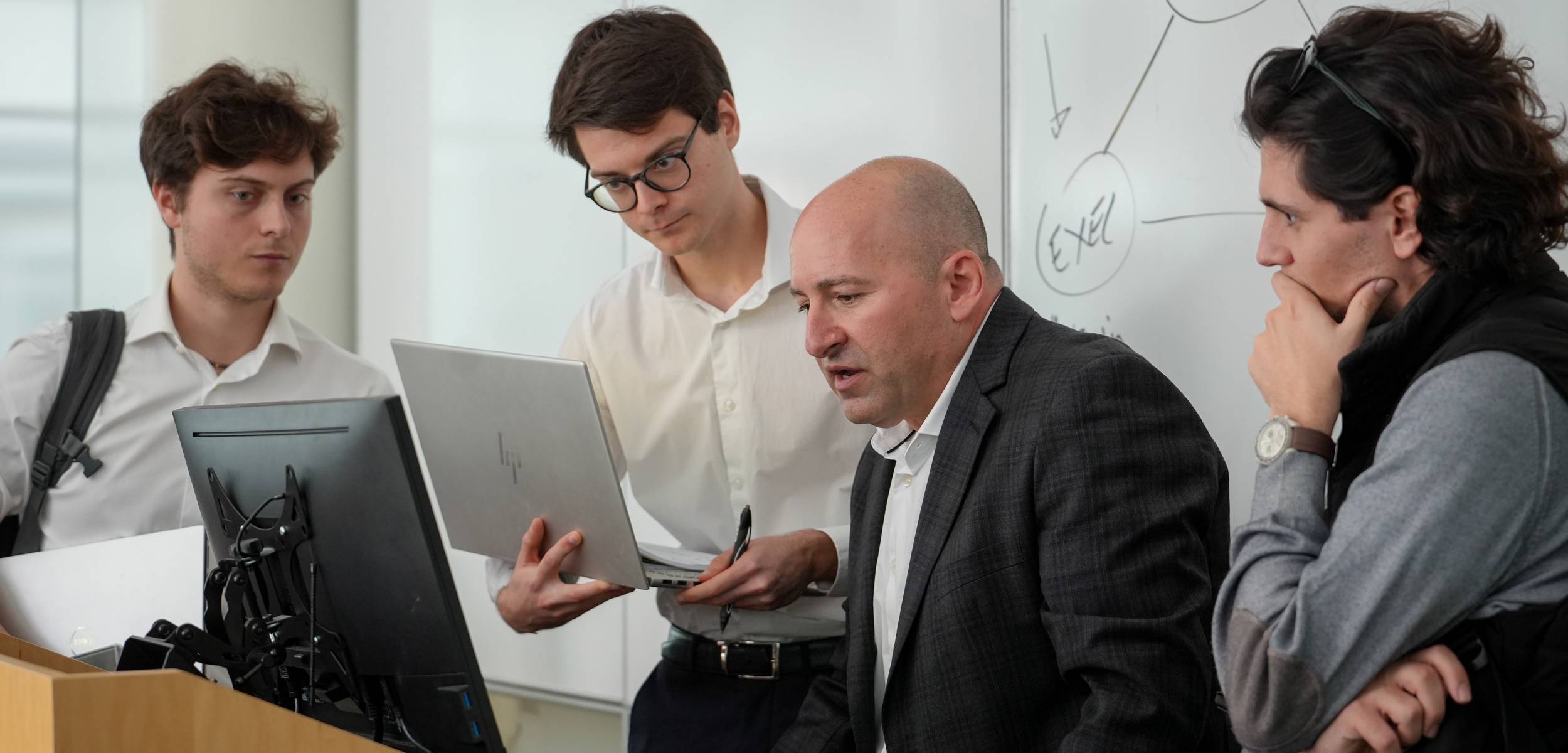 professor working on a computer with three students watching