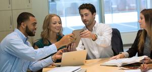 five students working on laptop, doing coursework, sitting at a table in