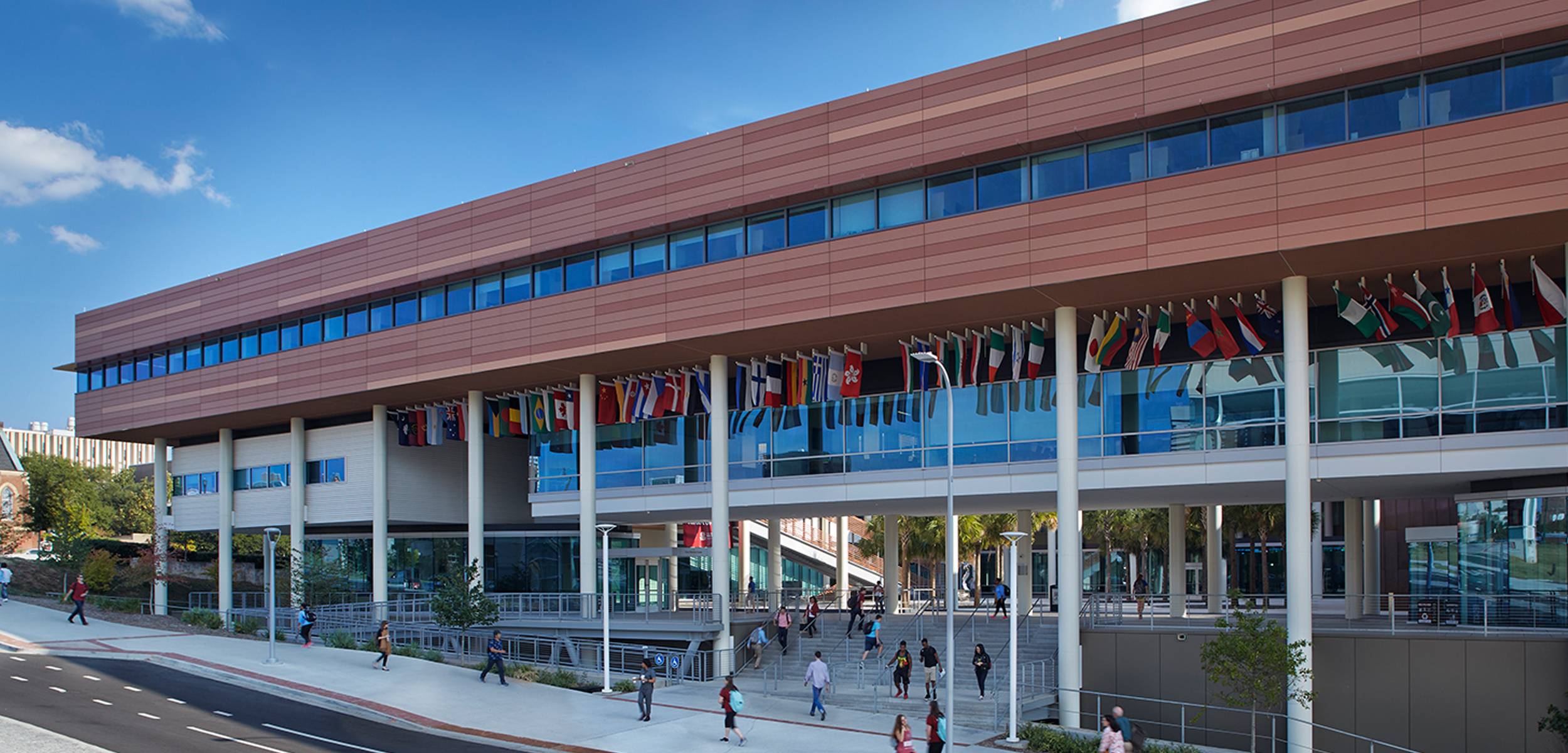 photo of the outside of the Moore School building, students walking, view of international flags hanging off the building