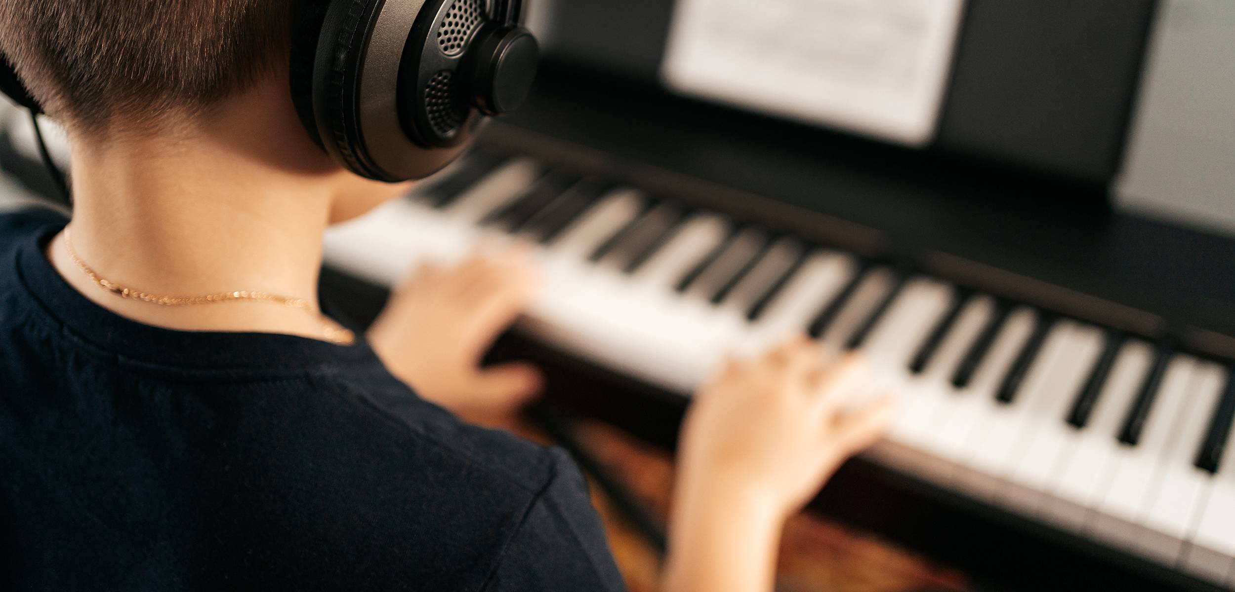 close up of young boy playing piano while listening to headphones
