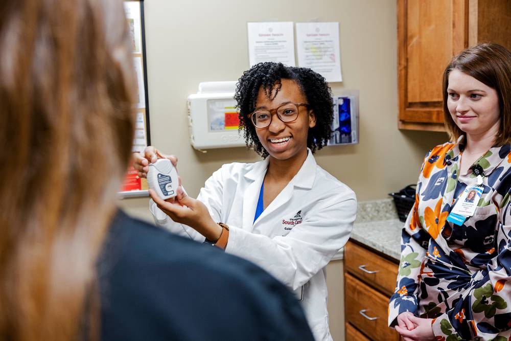 Student demonstrating a medication device to patient