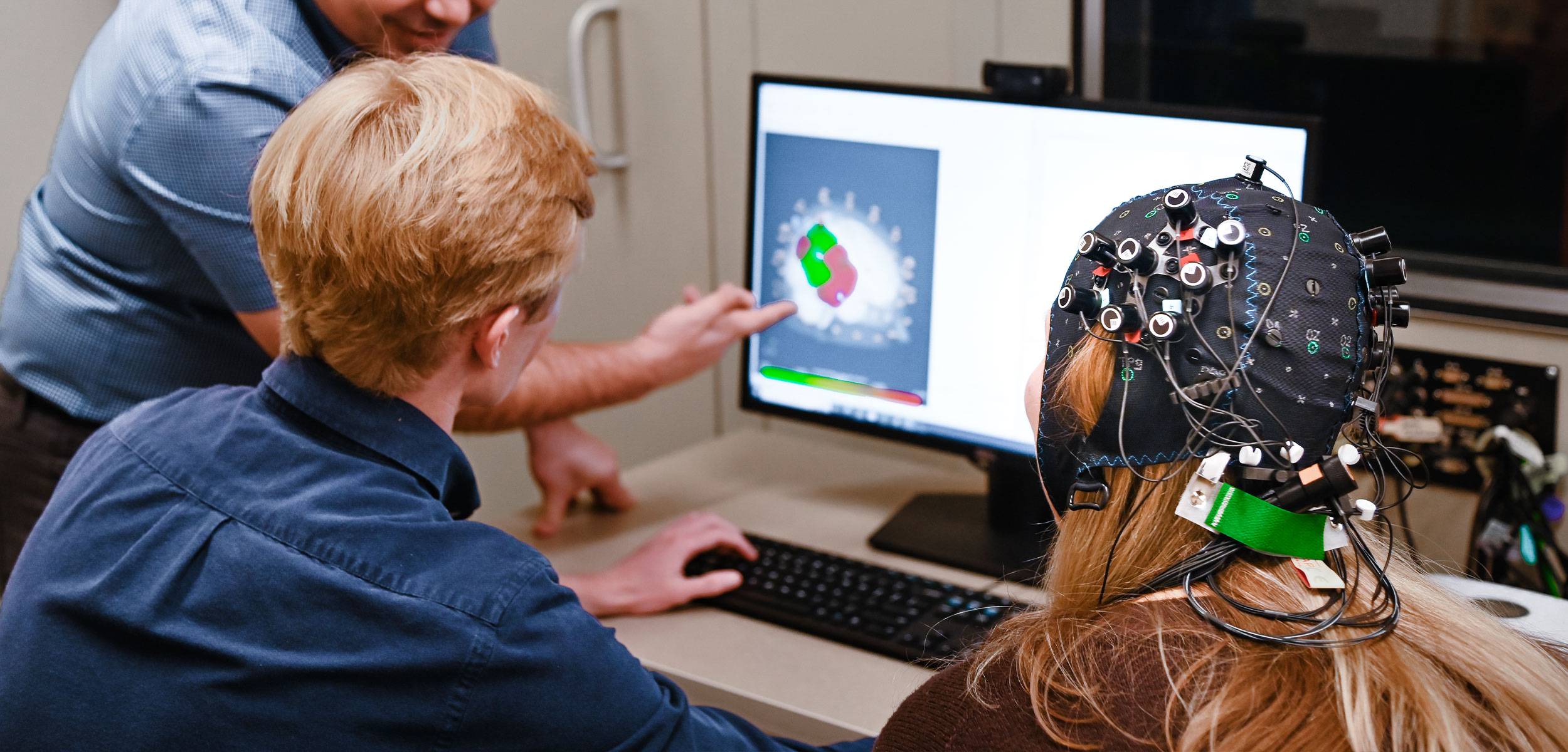 Professor and student with a brain cap on looking at monitoring on a computer screen