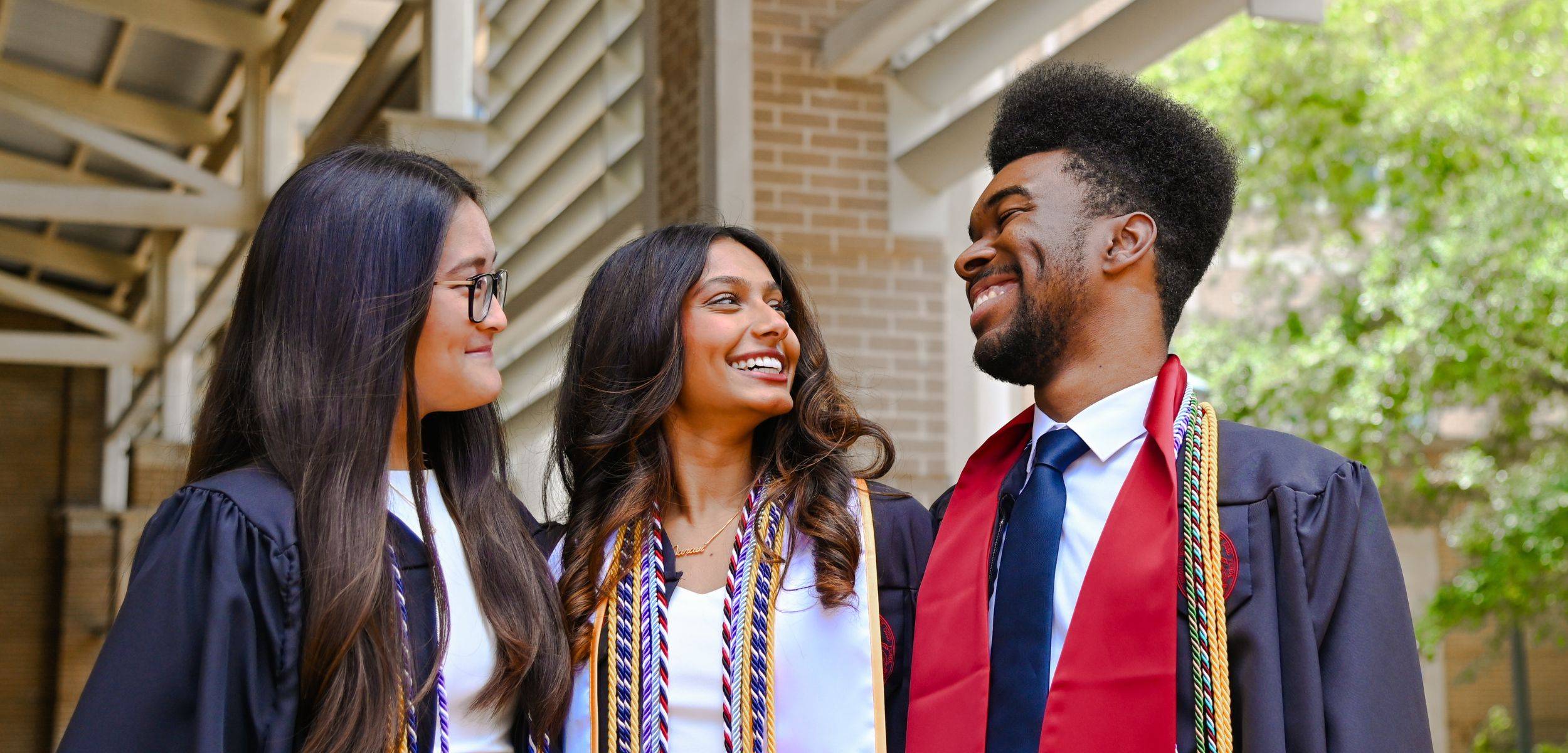 students in graduation robes smiling outside